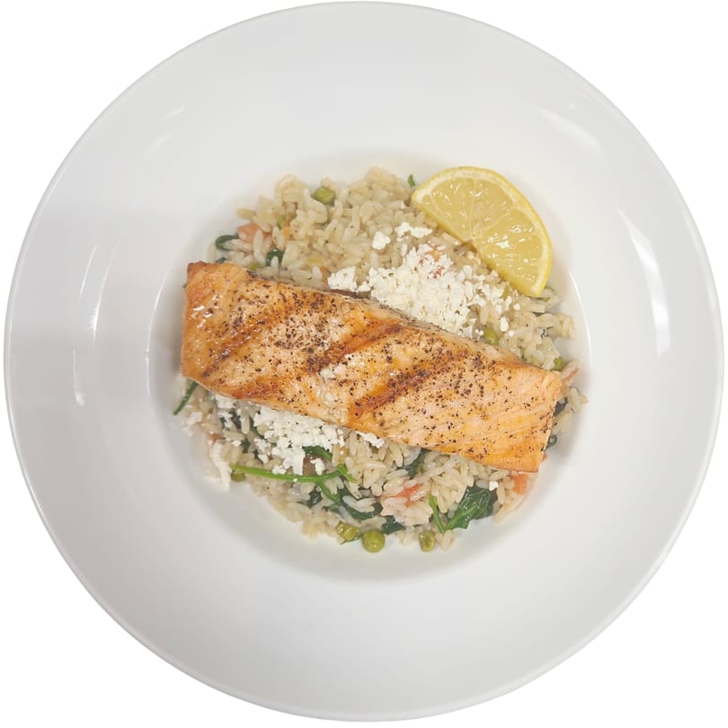 Grilled salmon fillet with rice, spinach, peas, feta cheese, and a lemon wedge on a white plate.