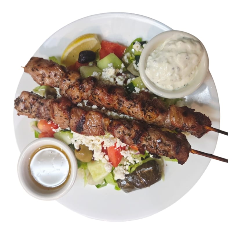Two grilled meat skewers with a Mediterranean salad, feta, olives, lemon, and two dipping sauces.