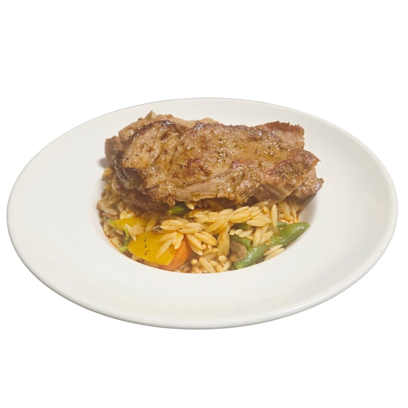 Grilled Mediterranean lamb chop served over orzo pasta with colorful vegetables on a white plate.