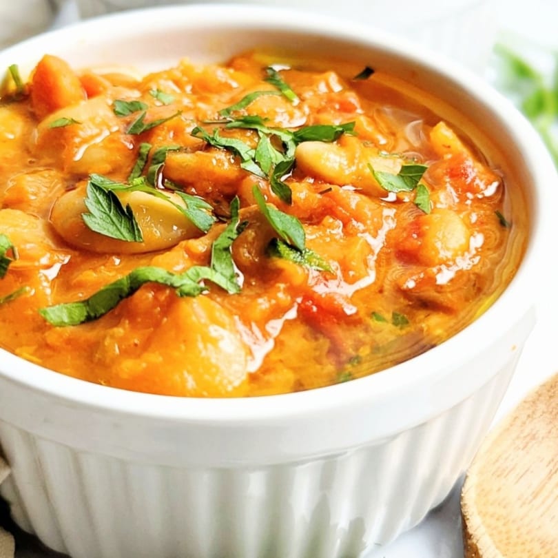 Close-up of a white bowl filled with a rich orange Mediterranean stew, garnished with fresh herbs.