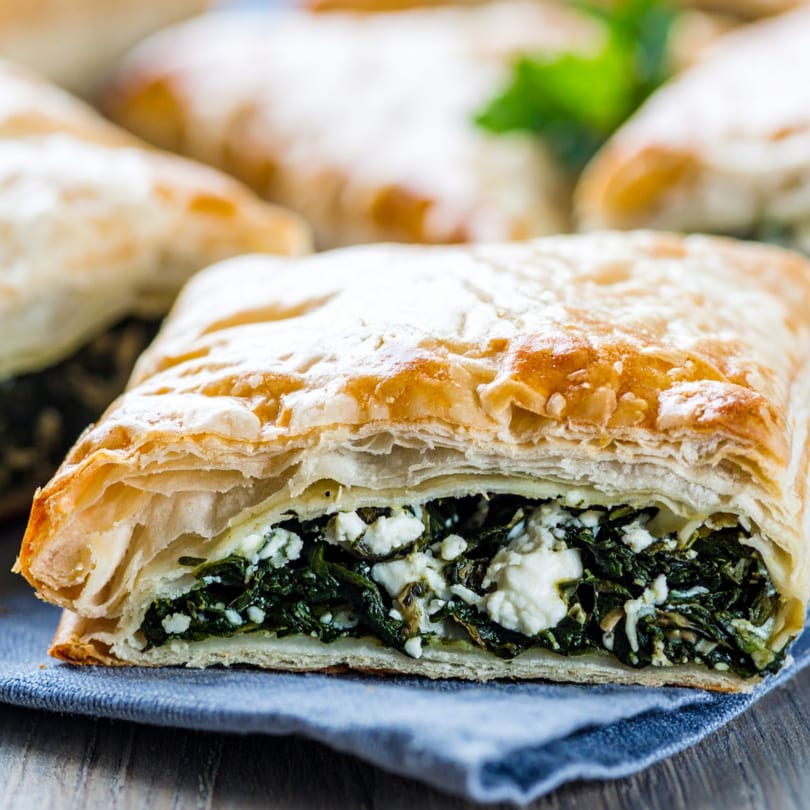 Close-up of a golden-brown spinach and feta pastry, revealing its flaky layers and savory filling.