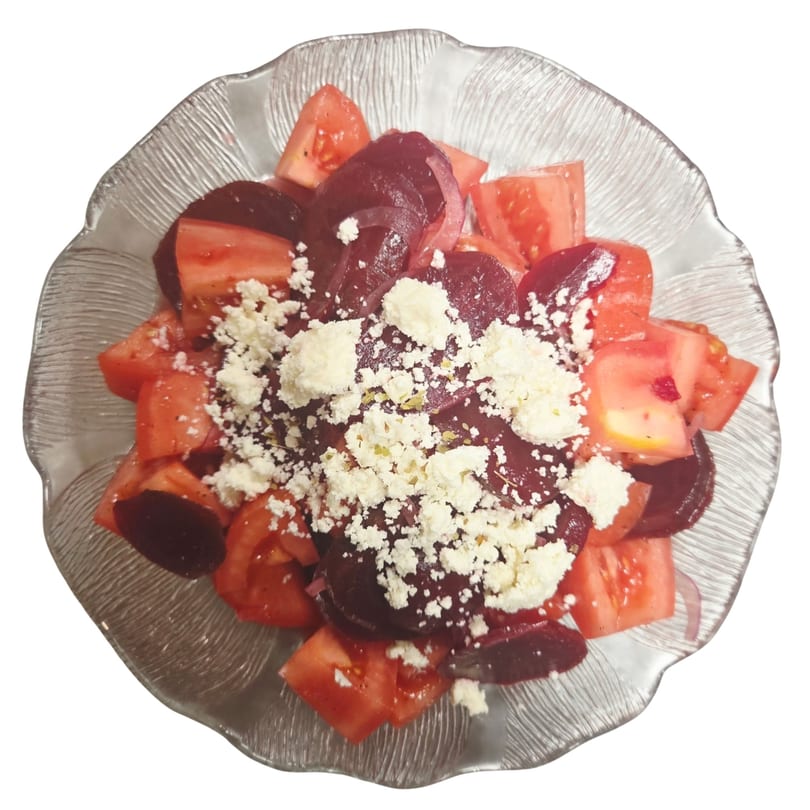 A Mediterranean salad with diced tomatoes, sliced beets, and crumbled feta cheese in a glass bowl.