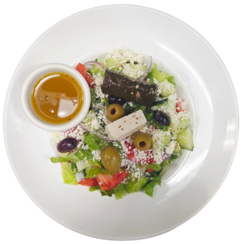 Mediterranean salad with lettuce, tomatoes, cucumbers, olives, feta, a dolma, and dressing on a white plate.